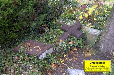 Umgefallener, bemooster Grabstein auf einem Friedhof mit Warnschild "Unfallgefahr"; Reparatur durch Steinmetzbetrieb Tauchert.